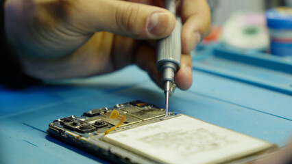 Close up of hands using a screwdriver to fix a mobile phone.