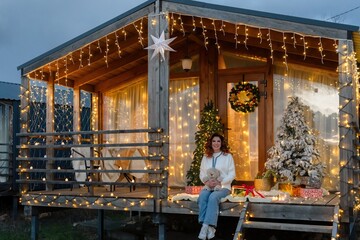 Christmas Lights Cabin Woman - A woman sits on a porch of a cabin decorated for Christmas.