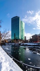 Towering skyscraper reflects sky, over a frozen river