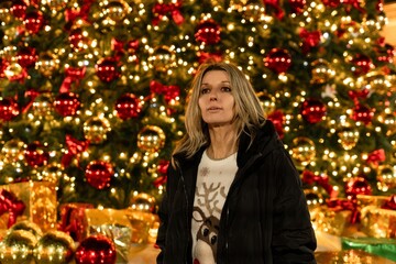 Woman Christmas Bokeh lights standing in front of giant festive tree decorations during winter holidays
