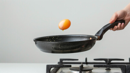 Woman hand holding black pan, egg dropping on pan,