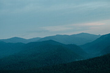 Obraz premium A view of blue distant mountains with wisps of fog after sunset, blue landscape