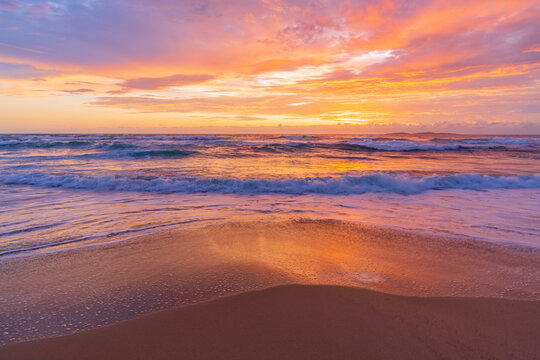 Dramatic colourful sunrise reflecting on a sandy coastal beach