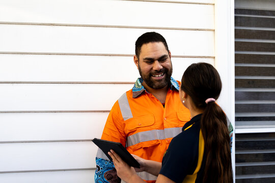 Father and daughter looking at a tablet outside a white weatherboard house