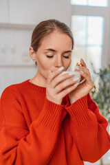 Woman coffee relaxation. Young woman in red sweater sipping hot morning beverage in kitchen.