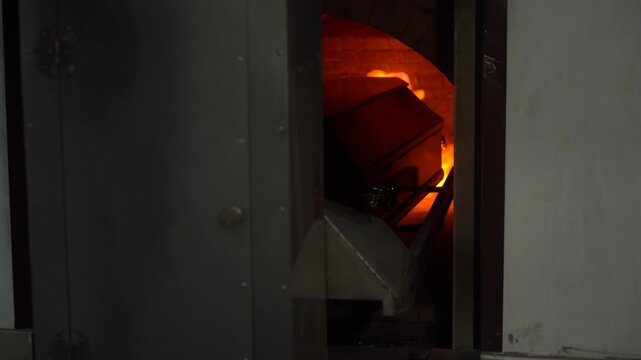 A coffin with a corpse is rolled into the flames of the crematorium and burned
