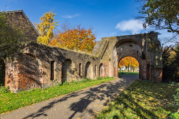 The ruins of the medieval city wall and Berkelpoort gate in Zutphen, Netherlands, surrounded by vibrant autumn foliage in a public park setting.
