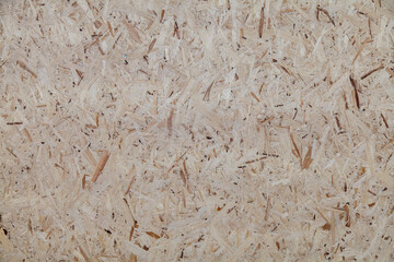 A close-up of a wood surface with a grainy texture. OSB. The surface is made of wood chips and has a rough, uneven surface.