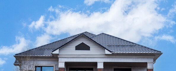 The roof of a house made of gray metal slate against the background of a sky with clouds