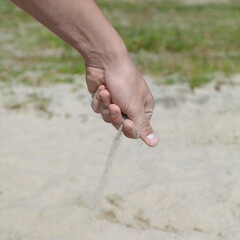 Hand is holding a handful of sand and sprinkling it on the ground. Concept of playfulness and relaxation, as the person is enjoying the simple act of playing in the sand