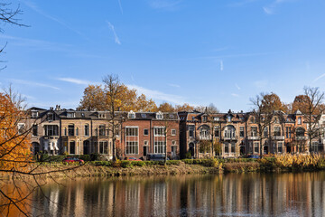 Stately historic mansions lining the water in Zutphen, Netherlands, perfectly reflected in the canal during a sunny autumn day with blue skies.