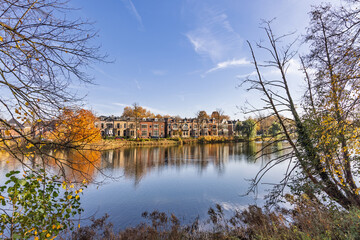 Scenic view of historic row houses along a canal in Zutphen, Netherlands, seen through a natural frame of tree branches during the autumn season.