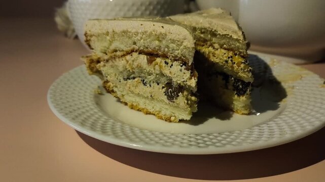 A piece of cake with cream in a plate on a pink table, a mug of tea and a kettle in the background. Tea party, snack. Sweet Cert