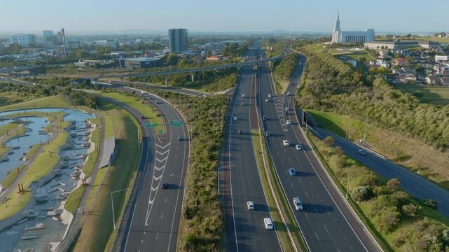 Aerial view of cars driving on a highway near Manukau in Auckland, New Zealand. The Auckland New Zealand Temple is visible in the background. The scene shows transportation and religion.