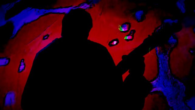 Man's silhouette musician playing electric guitar with psychedelic colors swirling about.