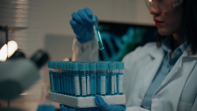 Young Asian woman researcher in a white coat analyzing a sample in a test tube. A professional microbiologist working in a medical lab