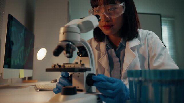 Young asian microbiologist looking through a microscope in a science lab. Medical researcher working with samples and developing a new drug