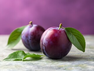 Obraz premium Two ripe purple plums with green leaves rest on a textured surface against a vibrant background