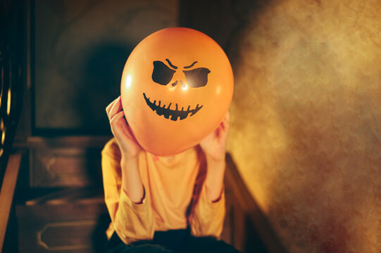 Child holding Halloween pumpkin balloon with scary face indoors