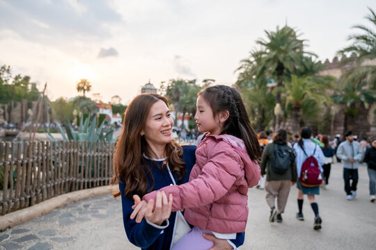 Asian mother and adorable daughter traveling together at theme park. 