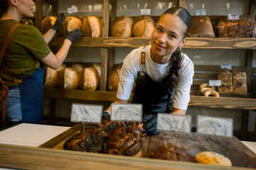 Smiling shop assistant in bakery arranging fresh bread and pastries