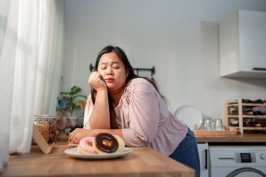 Asian plus-size woman looking tired while staring at a plate of donuts. 