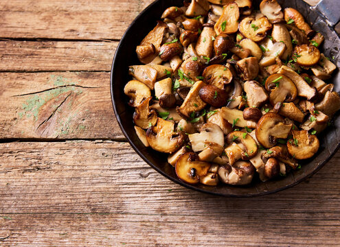 Fried mushroom and parsley in pan on rustic wood table