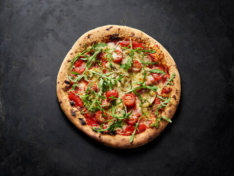 Neapolitan pizza with arugula tomato and mushroom on dark background