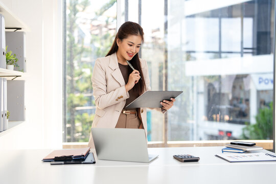 Smiling business woman working in office reading document. Professional manager holding paper finance report  at desk in office.