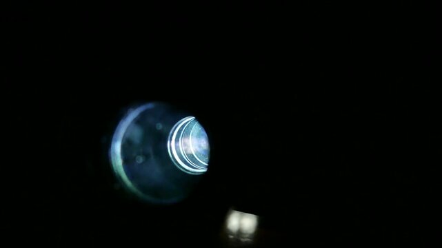 Dolly shot of the front lens of an operating vintage slide film projector, with sound.