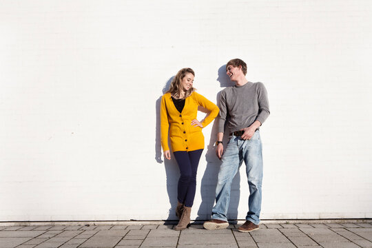 Smiling friends lean against wall in Munich wearing casual clothes