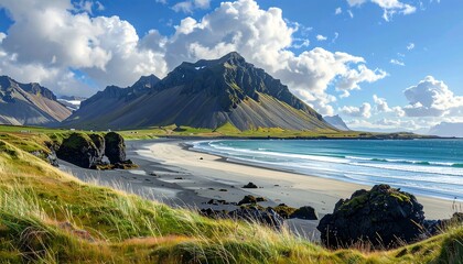 A coastal scene featuring a sandy beach, turquoise water, dark rocky cliffs, a majestic mountain, and a partially cloudy sky