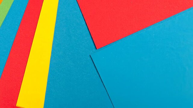 Colorful, angled sheets of paper in shades of green, red, yellow, and blue overlap in a patterned design