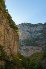 Naklejka premium Stunning canyon with steep, rugged cliffs covered in greenery, showcasing majestic beauty of nature under clear blue sky. Kabardino-Balkaria, Russia. Chegem Gorge 2024