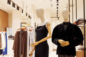 Two contemporary mannequins with wooden articulated arms showcase fashionable black dresses and blouses on display in a stylish retail clothing store environment