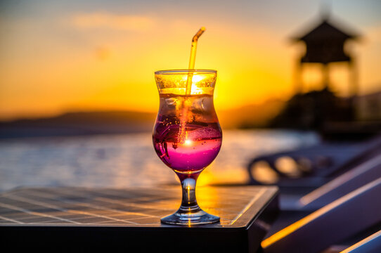 A cocktail glass stands by the pool against the sunset