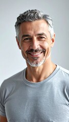 Portrait of a mature, smiling man with graying hair and a trimmed beard, wearing a casual gray t-shirt. The background is plain