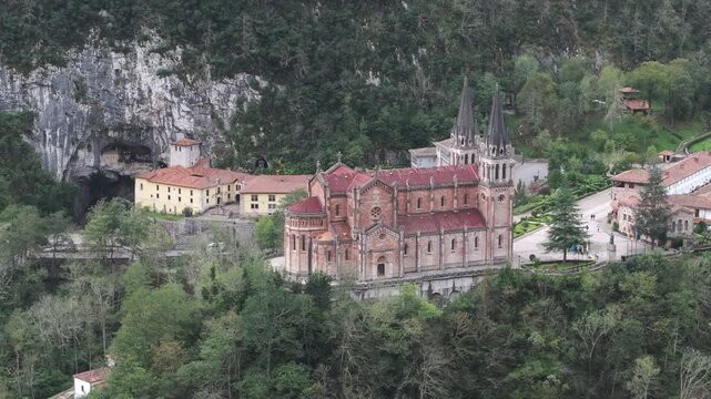 Cinematic aerial drone shot of the Basilica of Covadonga in lush forested mountains, iconic Catholic sanctuary and historic pilgrimage site in Asturias, northern Spain, Dramatic alpine landscape