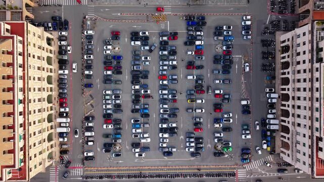 Static top down drone shot of an urban parking lot between residential buildings in central Genoa, showing parked cars and geometric city layout