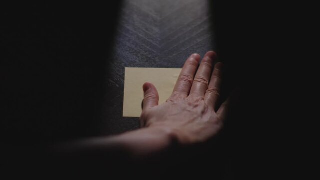 Slow motion close up footage of a hand writing out "June" on a paper note and placing it on a table. Shot in dramatic lighting for an impressive title or transition.