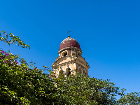 Church bell tower with a red dome above lush greenery in Corfu, Greece.  Monastery of Tenedos at old town.