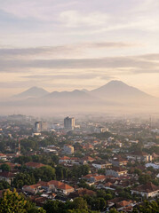 Panoramic view of Yogyakarta city with distant mountains, soft clouds, serene mood
