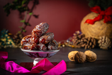 Close up of a dish of dates at Christmas with festive decorations and walnuts in shells