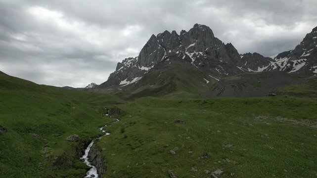 Aerial drone view high above a mountain river near Juta, Georgia, flowing through an alpine valley with rocky terrain and green slopes. Chaukhi Pass area and surrounding Caucasus mountains
