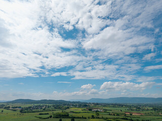 Wide landscape view of lush green countryside beneath vibrant, cloud-filled blue sky. 