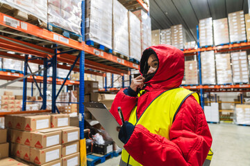 Worker in a cold storage warehouse checking inventory on a clipboard, managing supply chain in temperature controlled facility