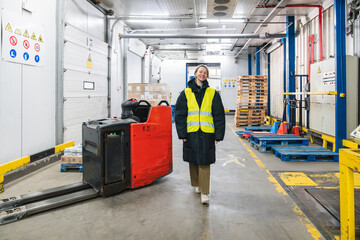 Woman smiling and walking towards a camera in a low temperature cold storage warehouse with a pallet jack