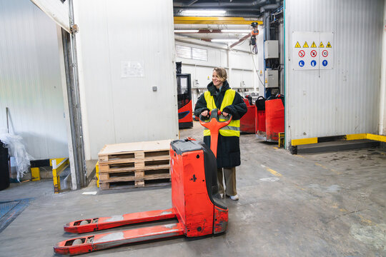 Female logistic worker in warm clothes operating an electric pallet jack, contributing to efficient cold chain management