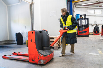 Worker operating an electric pallet truck in a low temperature cold storage logistics warehouse, wearing safety vest and warm clothing © Koldo_Studio