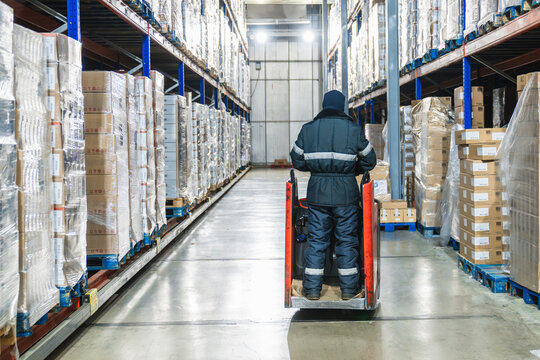 Worker in warm clothing moving pallets of goods with a forklift in a large low temperature cold storage facility - Powered by Adobe